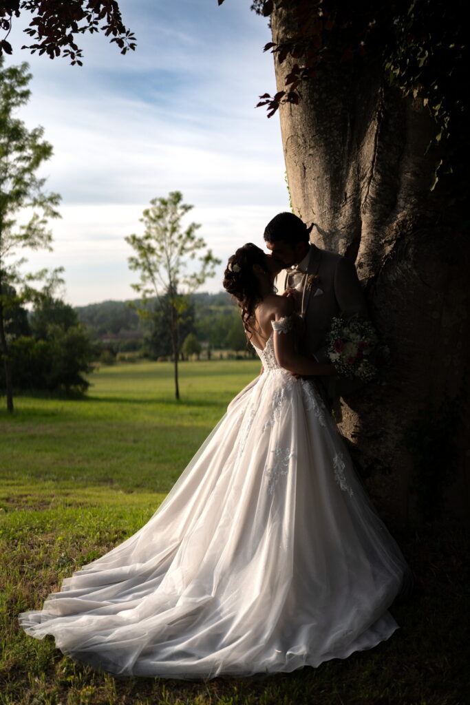 Mariés qui s'embrasse contre un arbre avec la robe de la mariée magnifique