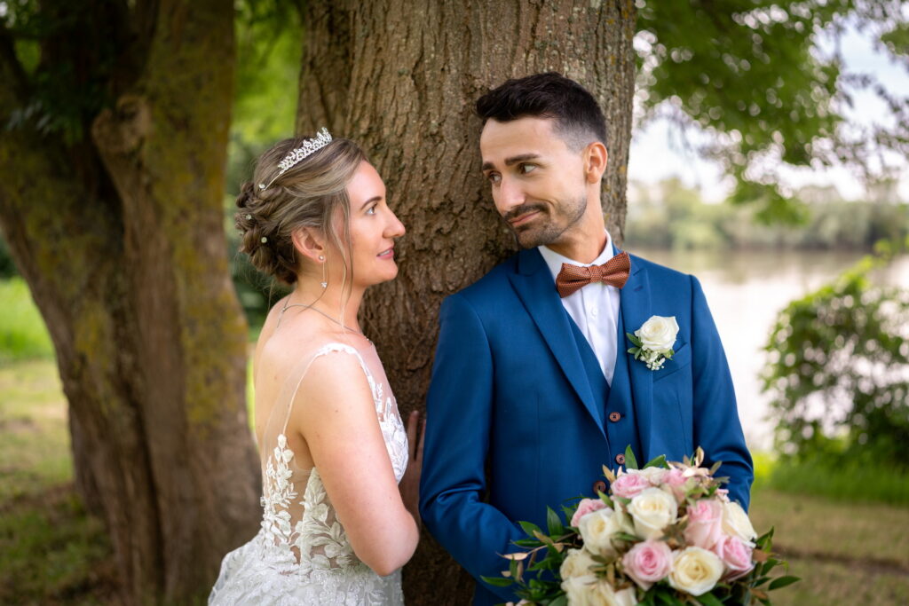 Mariés se regardant en souriant près d’un arbre, bouquet à la main aux Domaines de Gaston