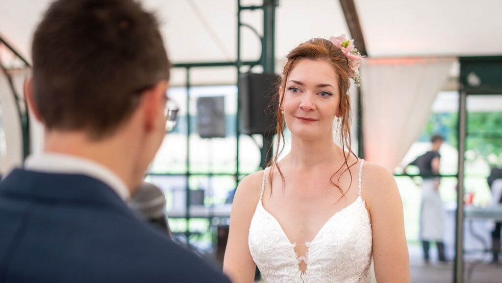 La mariée, émue et les larmes aux yeux, écoute les mots du marié pendant la cérémonie laïque au Domaine de la Butte Ronde