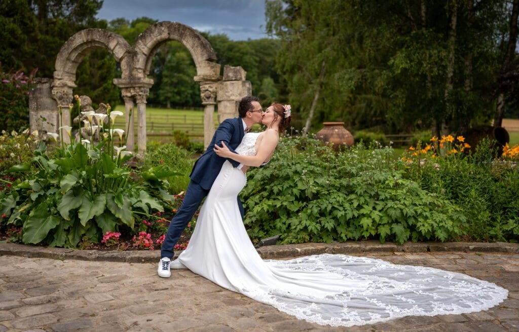 Les mariés s’embrassent au Hameau du Domaine de la Butte Ronde, la mariée se penche avec sa robe à traîne