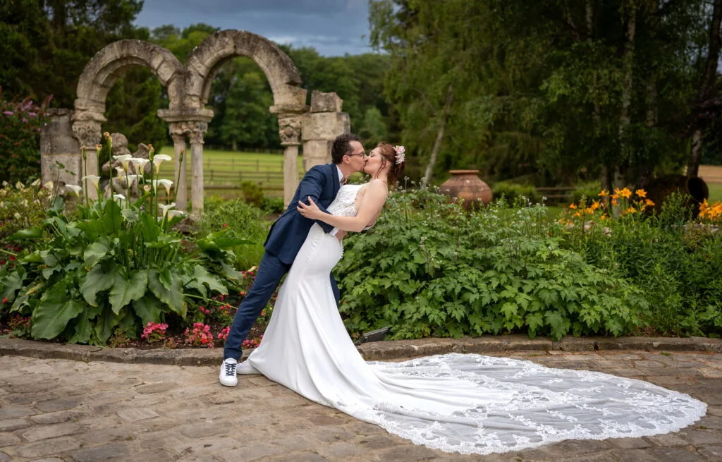 Les mariés s’embrassent au Hameau du Domaine de la Butte Ronde, la mariée se penche avec sa robe à traîne